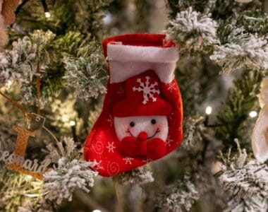 Small red snowman Christmas stocking hanging on a flocked tree beside a personalized name ornament