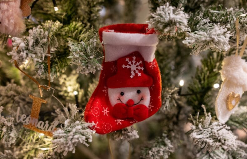 Small red snowman Christmas stocking hanging on a flocked tree beside a personalized name ornament
