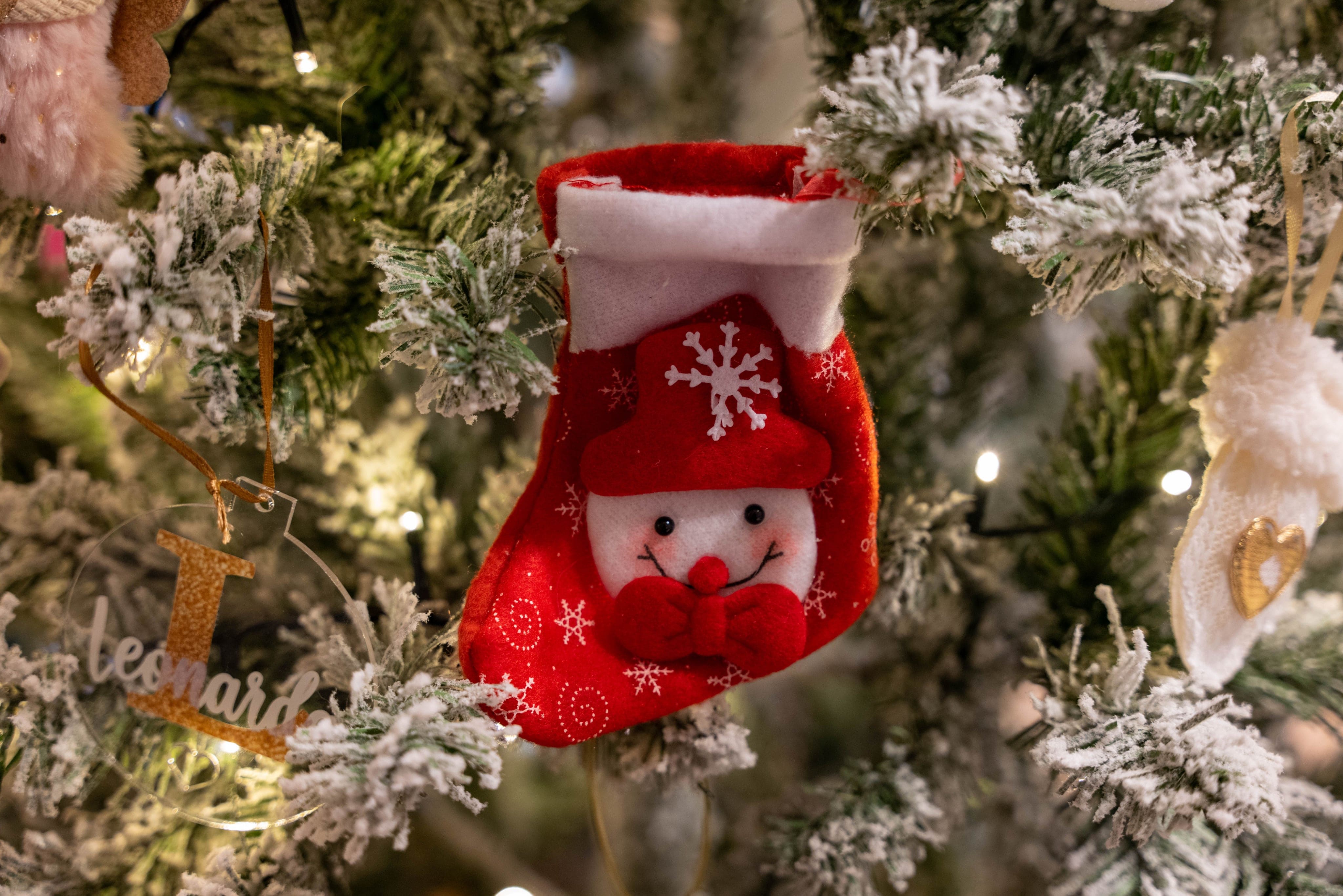 Small red snowman Christmas stocking hanging on a flocked tree beside a personalized name ornament