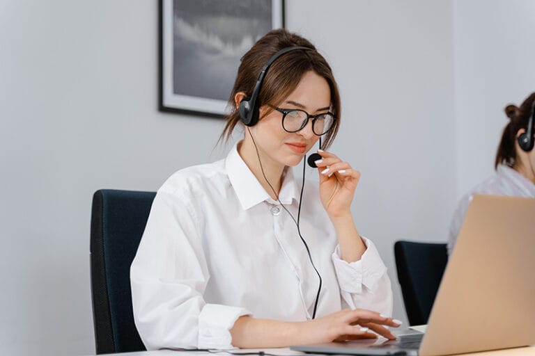 Customer service agent wearing a headset and glasses, working at a laptop in an office