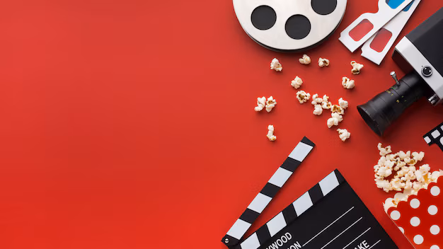 Film reel, 3D glasses, a movie camera, a clapperboard and scattered popcorn arranged on a red background