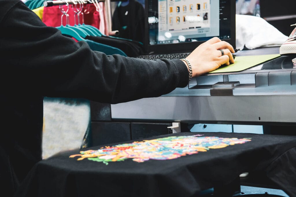 Operator guiding a black t-shirt through a direct-to-garment printer as a colorful design is printed