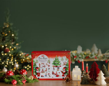 Red illustrated Advent calendar box standing on a wooden table among toadstool ornaments, pinecones, candles and paper trees